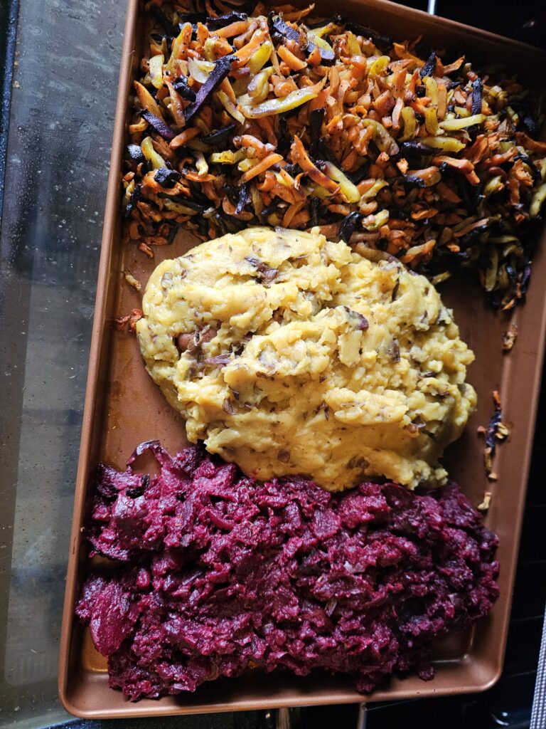 The roasted carrots, mashed potato, and macerated beets staged on the tray from roasting the carrots