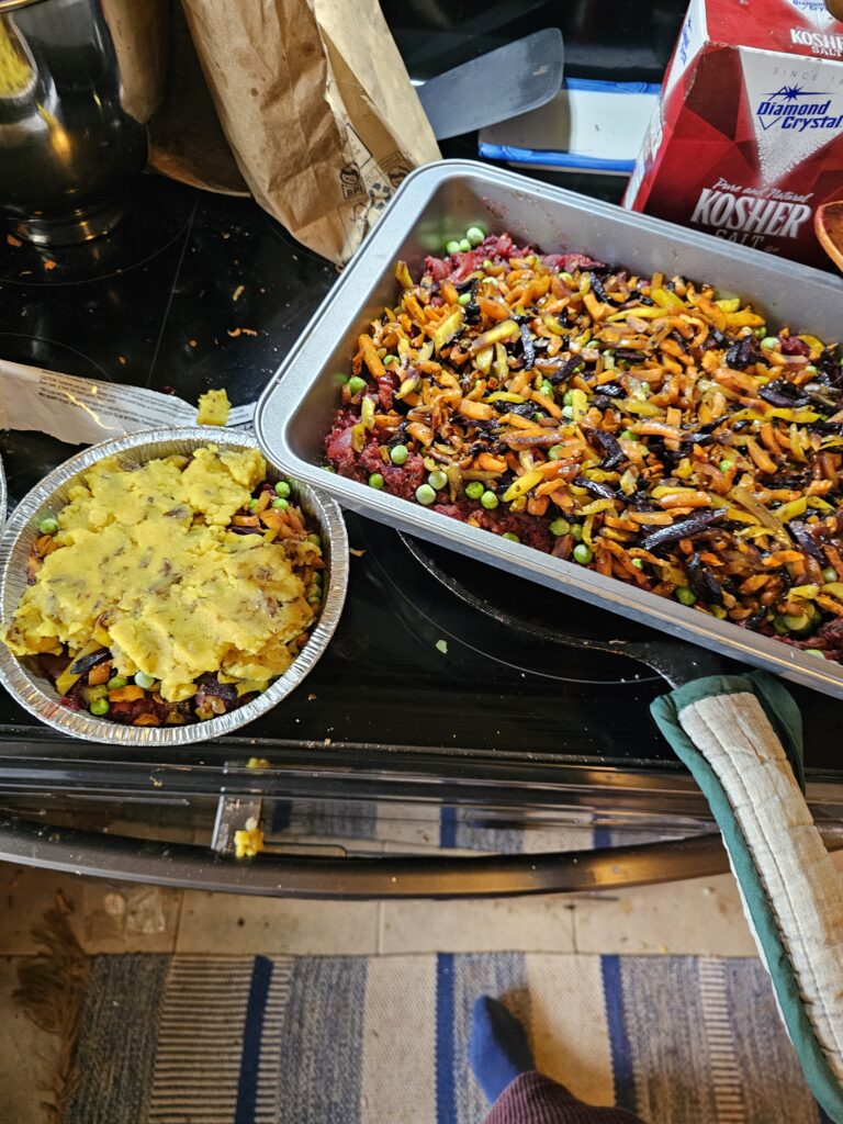 A small samosa pie is beginning to have potato added to its top, while the large samosa pie shows the carrots and peas layered over the beets