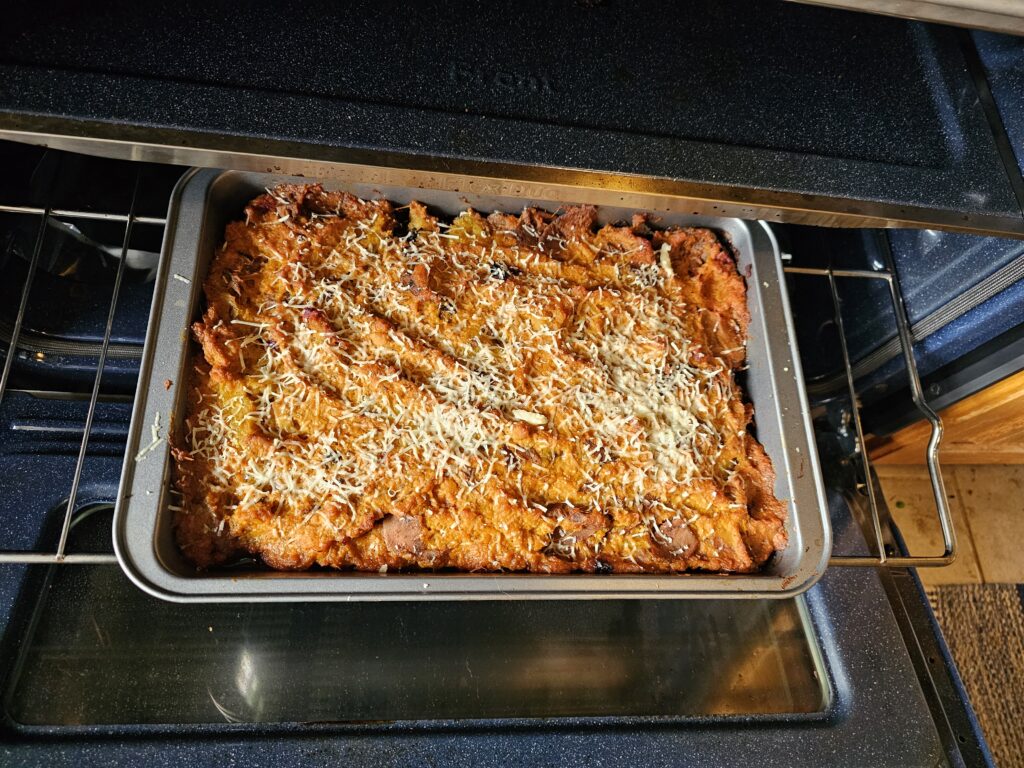 The sweet potato version of samosa cottage pie on the oven tray. There is cheese on top.
